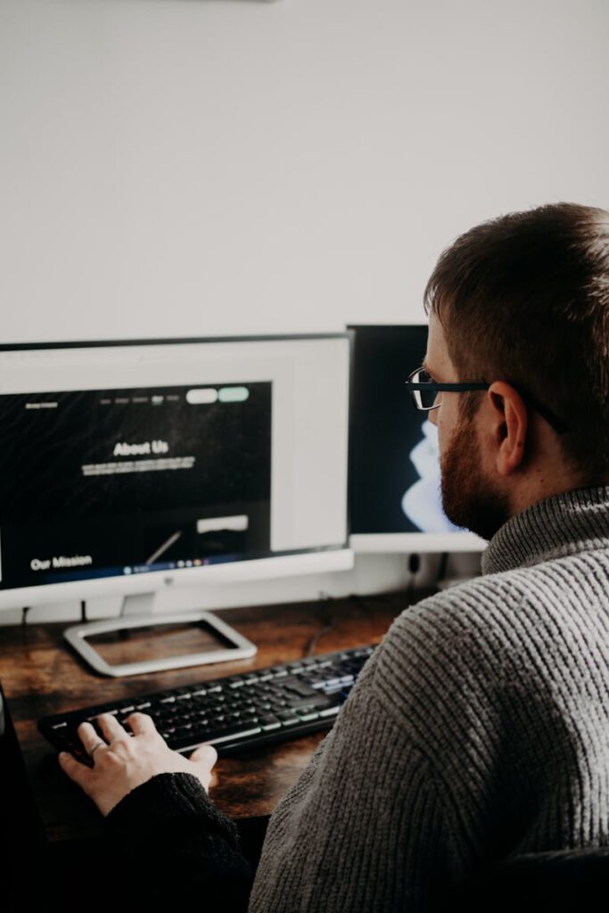Man working on web design at home office setup with dual monitors.