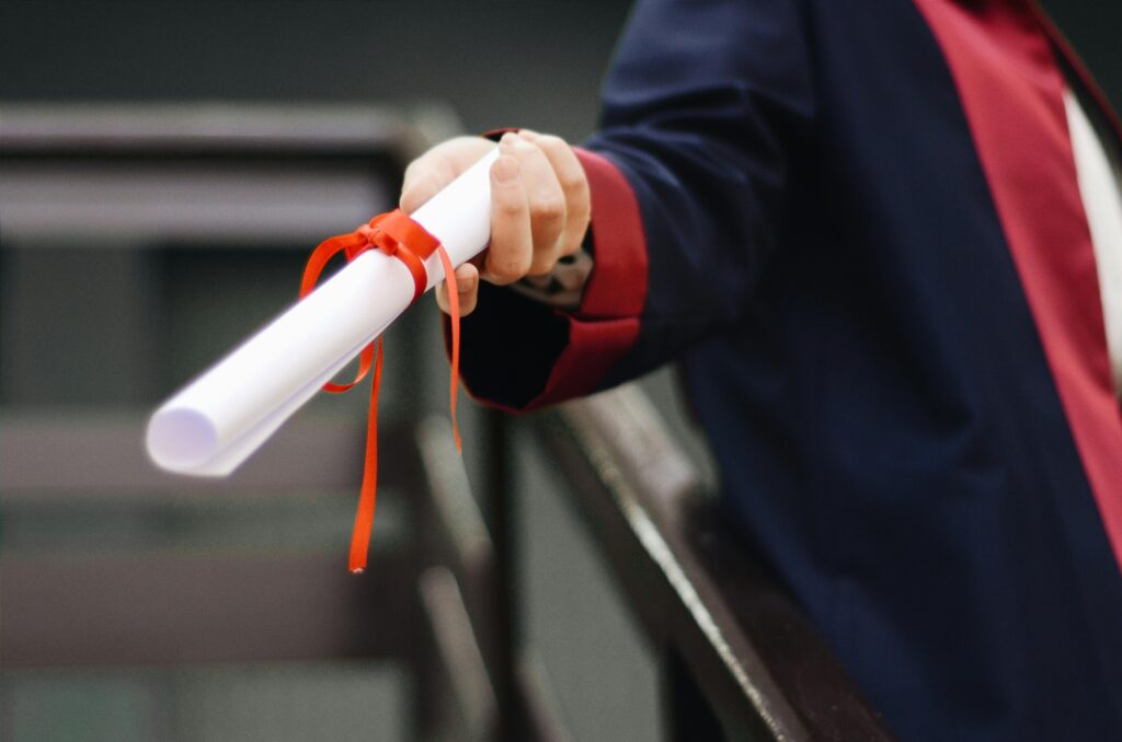 Tuition & Aid A close-up image of a graduate holding a diploma tied with a red ribbon, symbolizing achievement and success.