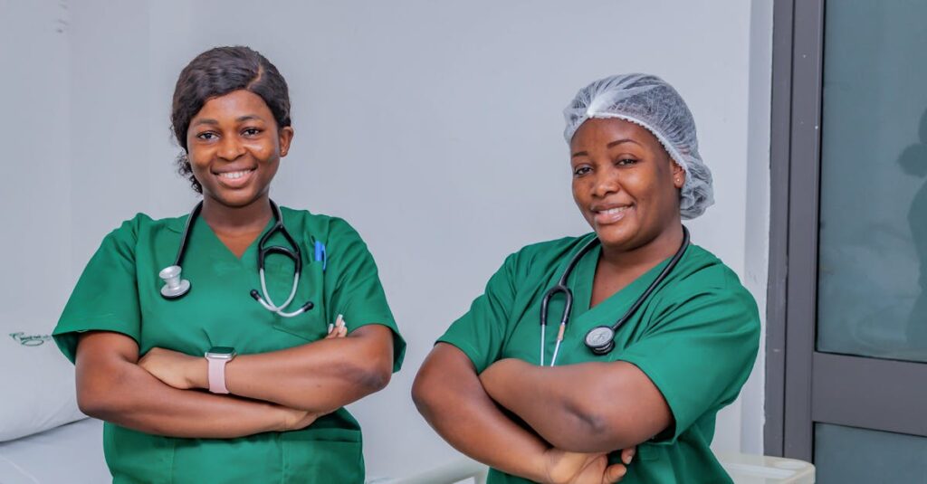 Two female nurses in green scrubs smiling confidently in a hospital room. Professional healthcare workers.