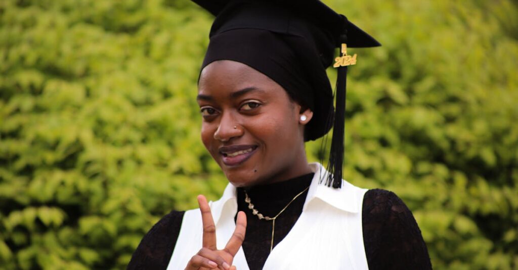 Black female graduate holding peace sign in outdoor ceremony, Albany, NY.