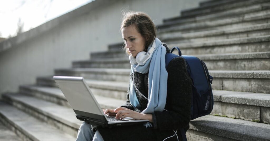 Certificate Programs Woman using laptop on outdoor stairs, studying online with headphones and backpack.