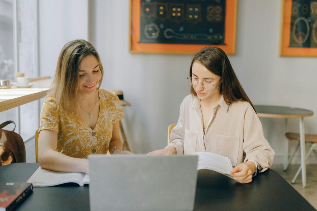 Two young women studying together in a cafe with a laptop and books.