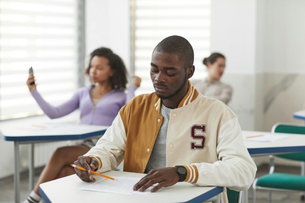 A student concentrating on an exam in a classroom setting, holding a pencil.