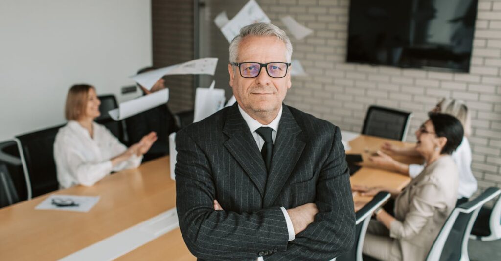 Master's Degrees Business executive standing confidently in meeting room with team engaged in discussion behind.