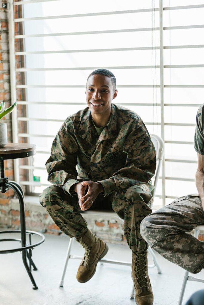 A smiling female soldier in military uniform sitting indoors, conveying warmth and bravery.