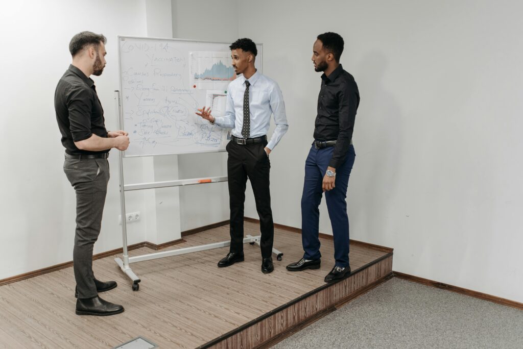Three professionals engage in a business discussion in an office with a whiteboard.