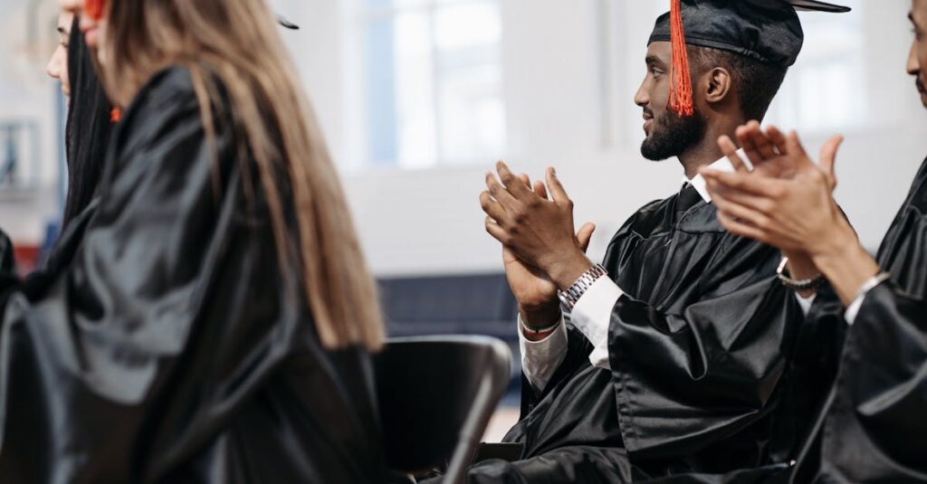 Graduates in caps and gowns clapping during a joyful graduation ceremony indoors.