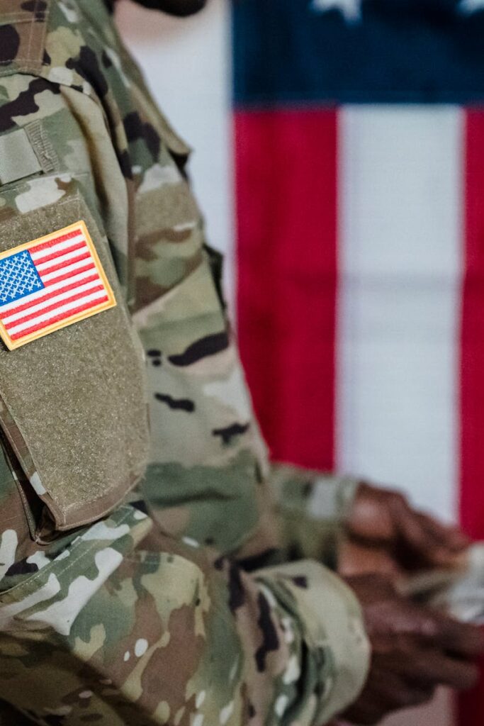 Close-up of a soldier in military uniform with American flag patch and background.