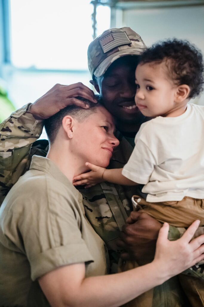 A heartwarming moment of a family reunion with a soldier in uniform holding a child indoors.
