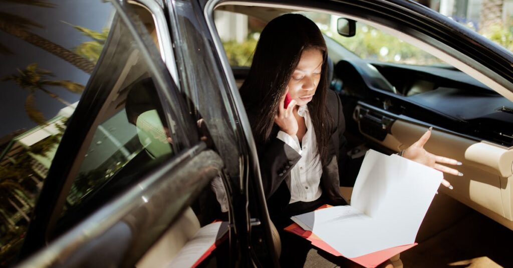 A businesswoman multitasking with phone and documents while seated in a car.