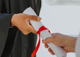 Cost of Attendance Hands exchanging a graduation diploma wrapped with red ribbon, symbolizing achievement.
